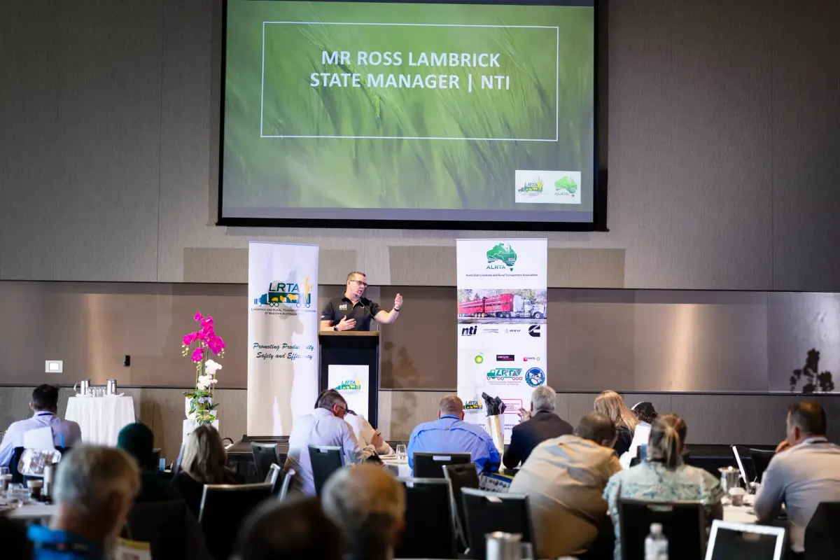 Conference speaker addressing delegates beside a presentation screen at LRTAWA Corporate Event.