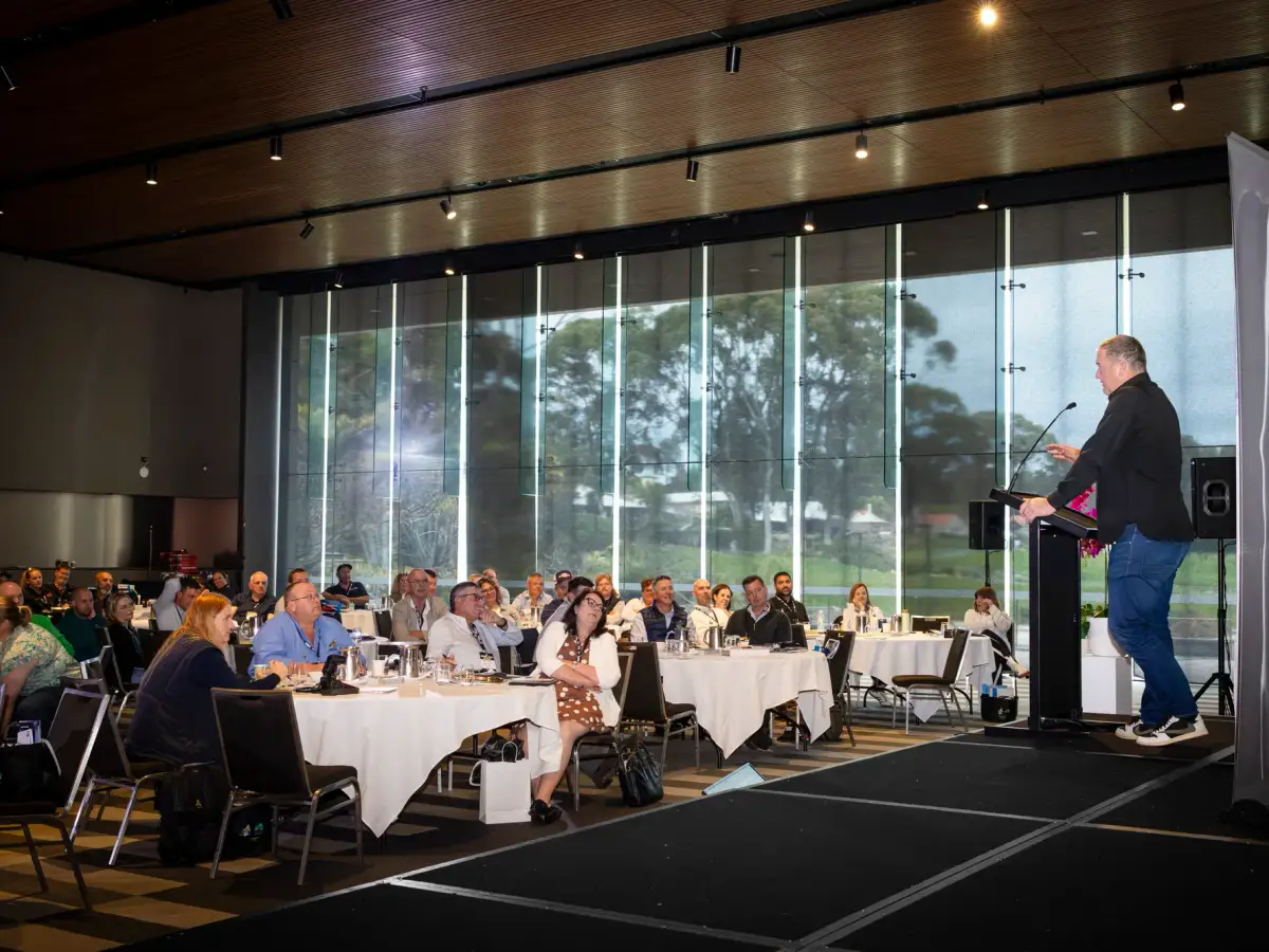 Speaker addressing a seated audience in a bright conference room at LRTAWA Corporate Event.