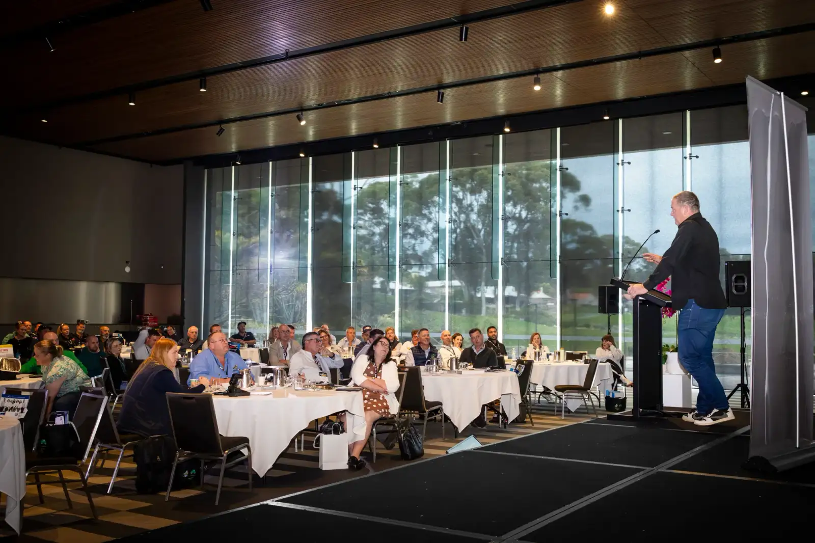 Speaker addressing a seated audience in a bright conference room at LRTAWA Corporate Event.
