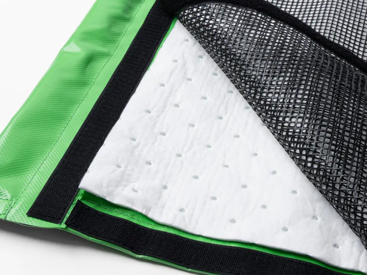 Close-up of the Lubie spill-containment mat showing its green edge, black mesh, and white absorbent layer