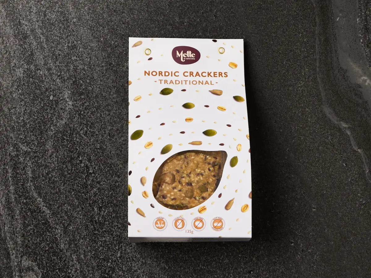 Mette is Baking Traditional Nordic Crackers retail box with seed-print packaging photographed on a dark stone surface