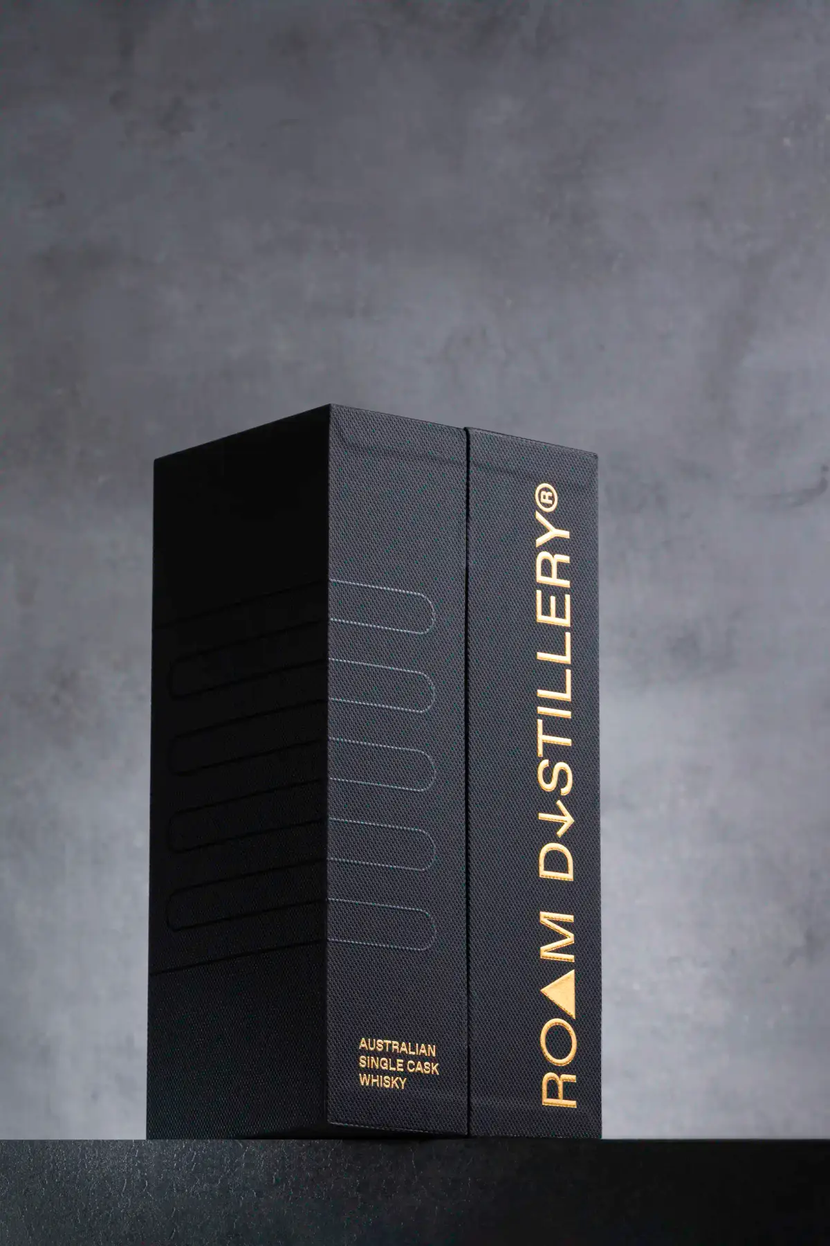 Black Roam Distillery rigid packaging box with gold foil branding photographed upright on a dark studio background