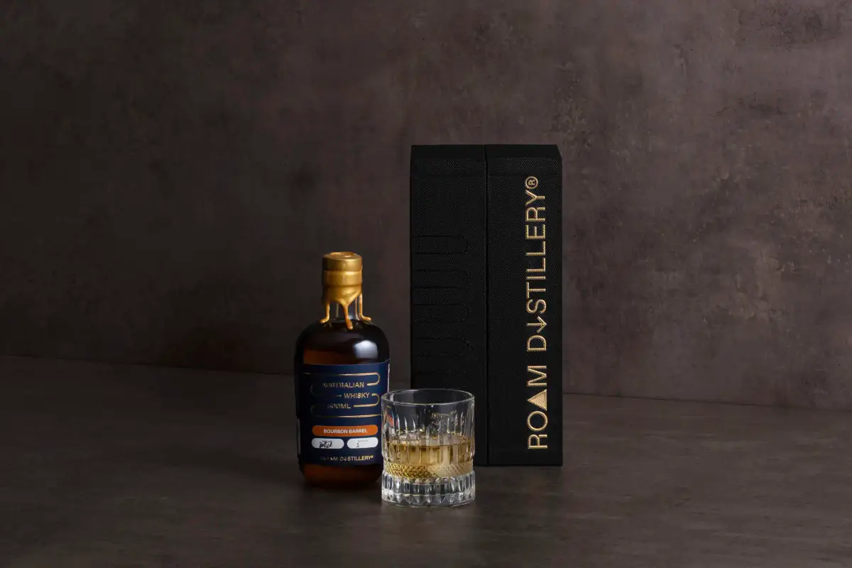 Roam Distillery whisky bottle and glass styled beside a black rigid presentation box with gold foil branding by Myerton Packaging