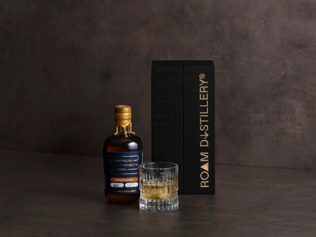Roam Distillery whisky bottle and glass styled beside a black rigid presentation box with gold foil branding by Myerton Packaging