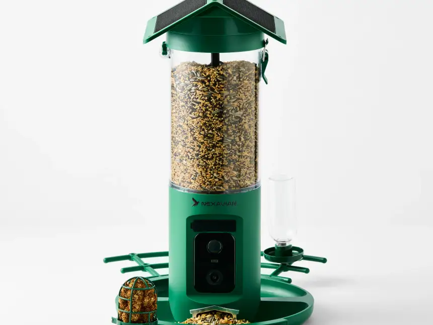 Green Nexavian camera bird feeder filled with seed, with its roof, front camera and feeding attachments visible on a light background