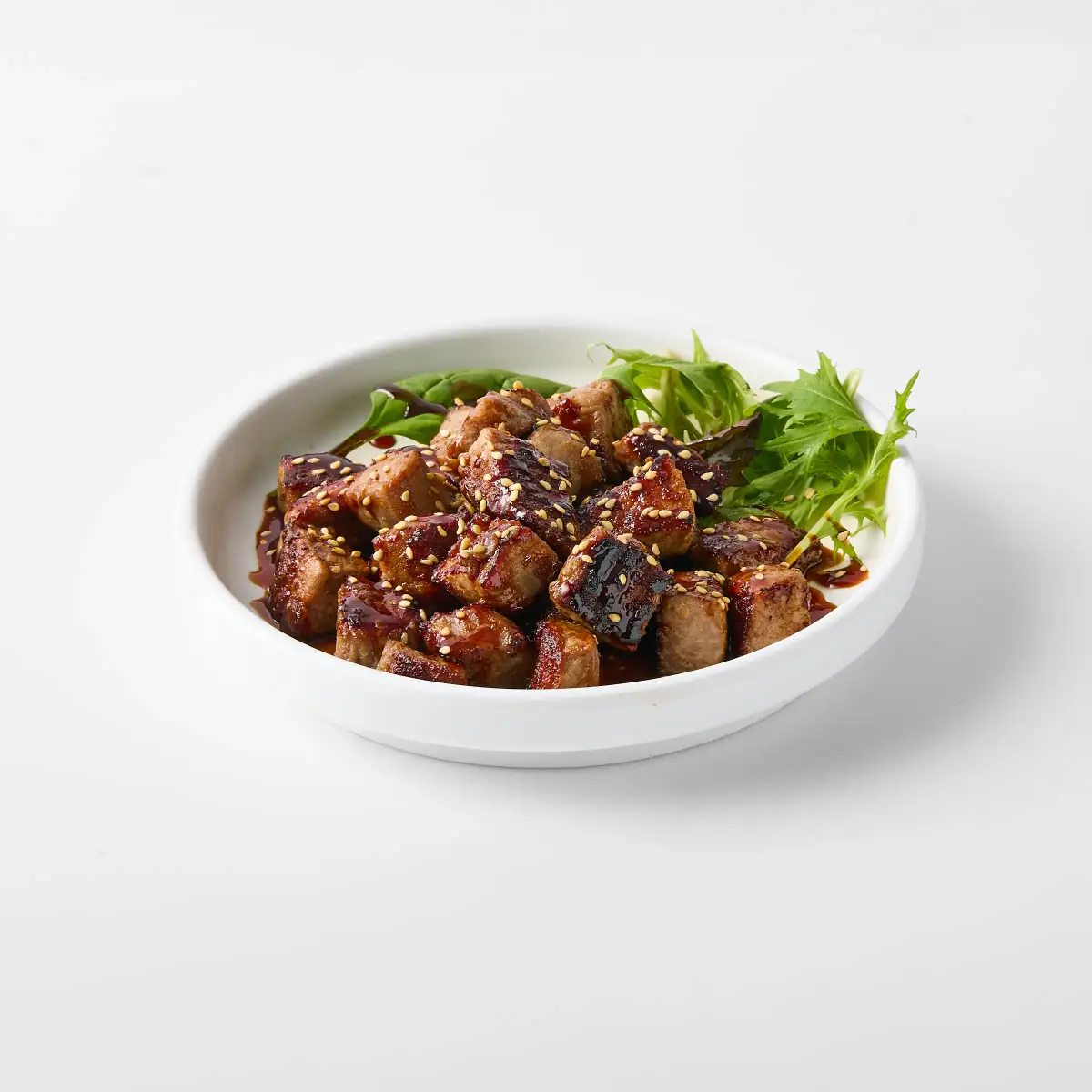 Omasa Japanese Restaurant beef dish glazed with dark sauce and sesame seeds, plated with mixed greens on a white background