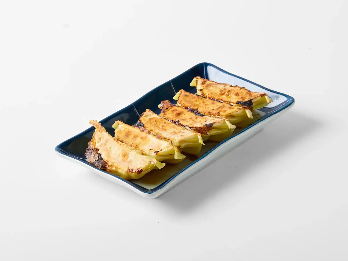 Close-up menu photo of Omasa Japanese Restaurant chicken gyoza on a blue rectangular plate against a white background