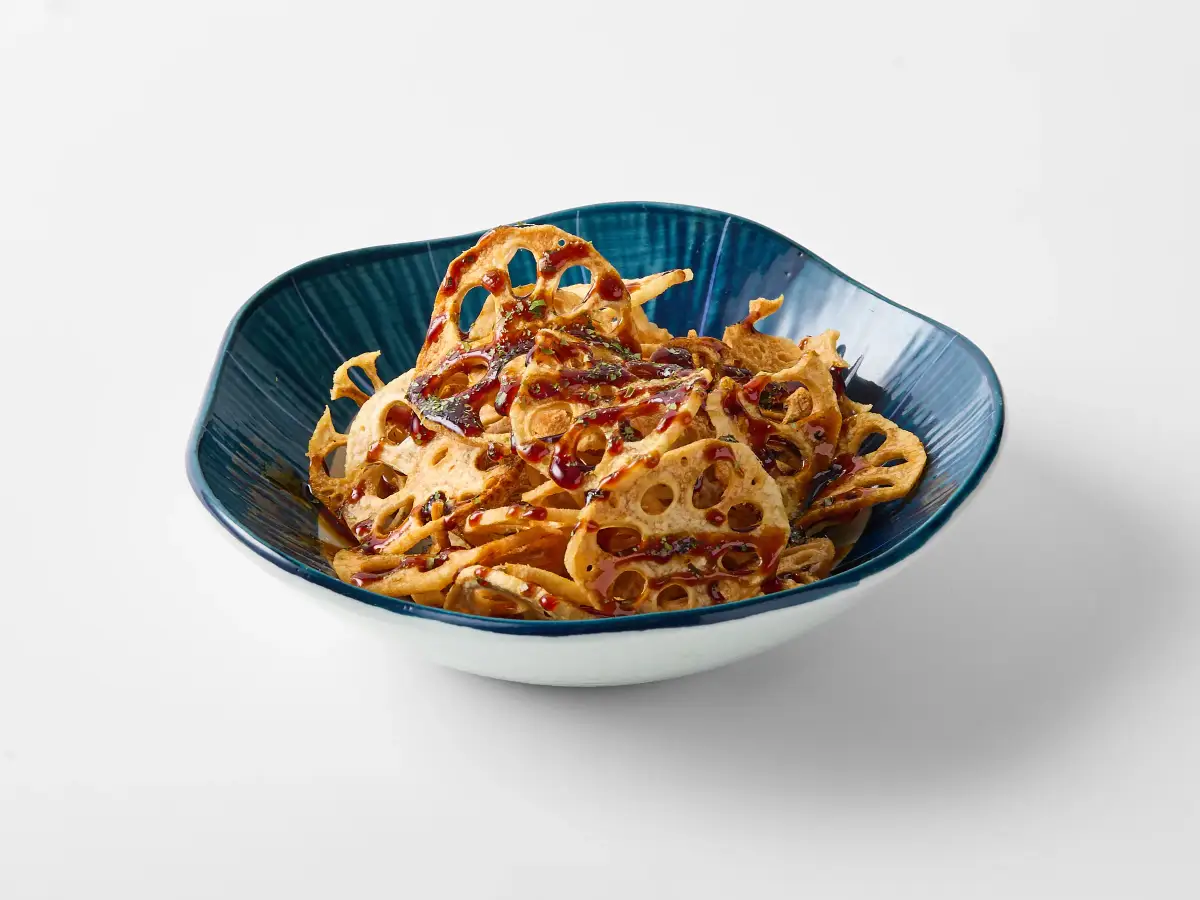 Crisp lotus root chips from Omasa Japanese Restaurant drizzled with sauce in a blue bowl on a white background