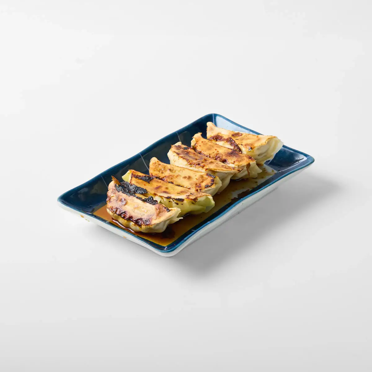 Pan-fried gyoza from Omasa Japanese Restaurant lined on a rectangular plate with dipping sauce on a white background