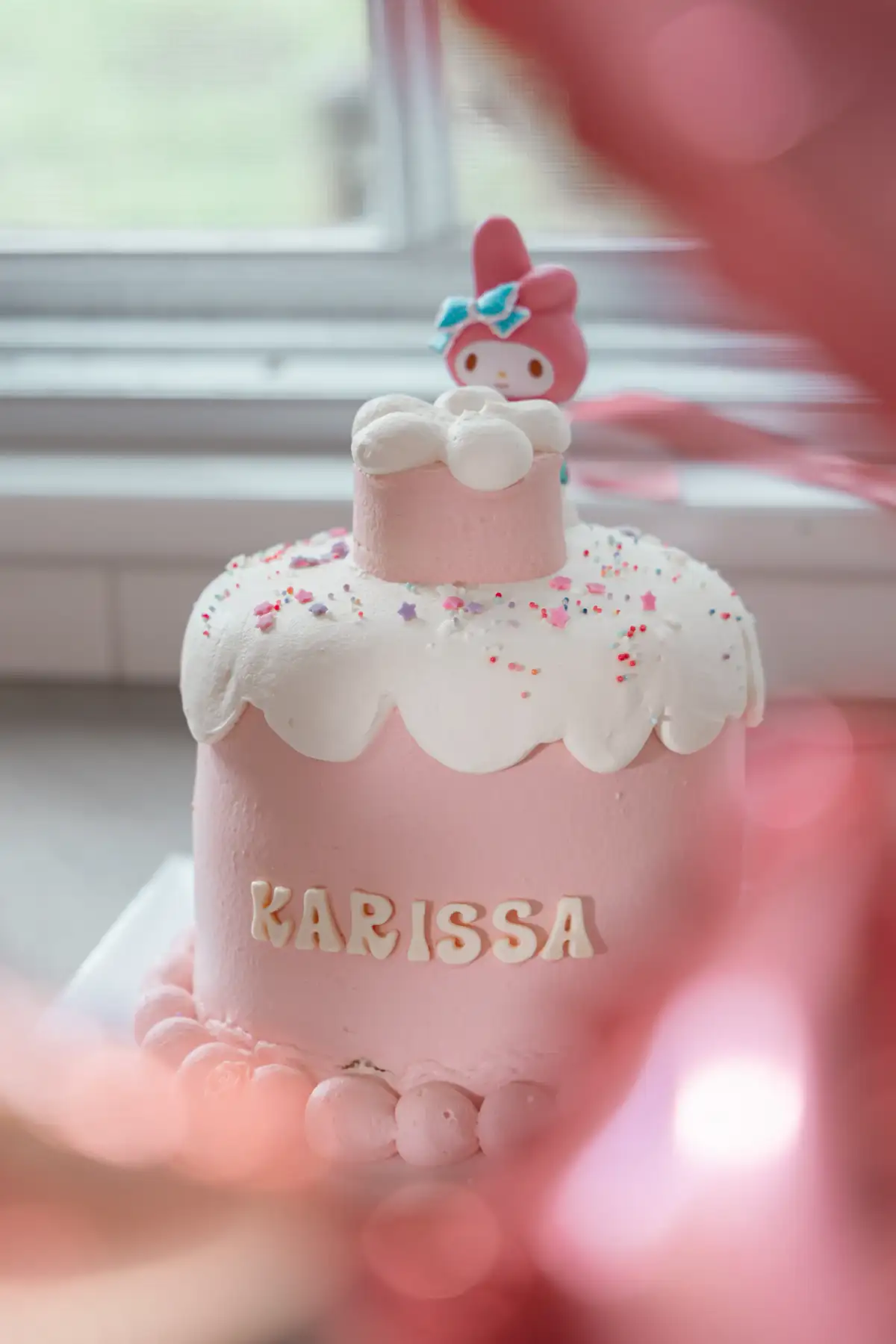 Pink birthday cake photographed among the party decorations.