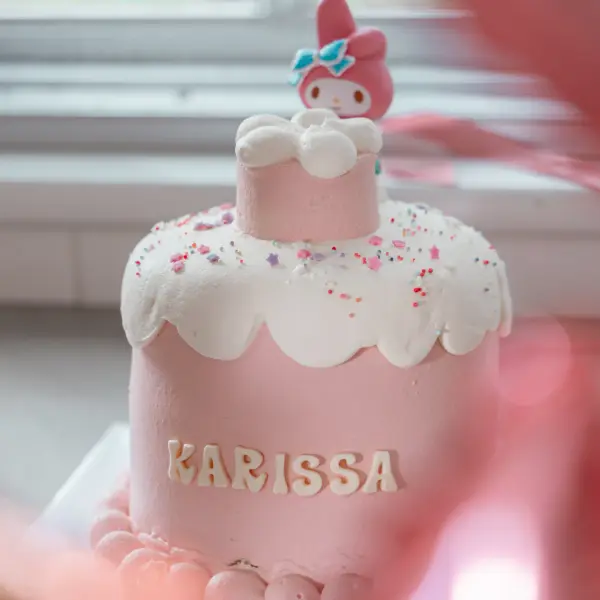 Pink birthday cake photographed before guests gathered around it.
