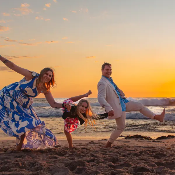 Family sharing a playful candid moment on the beach at sunset.