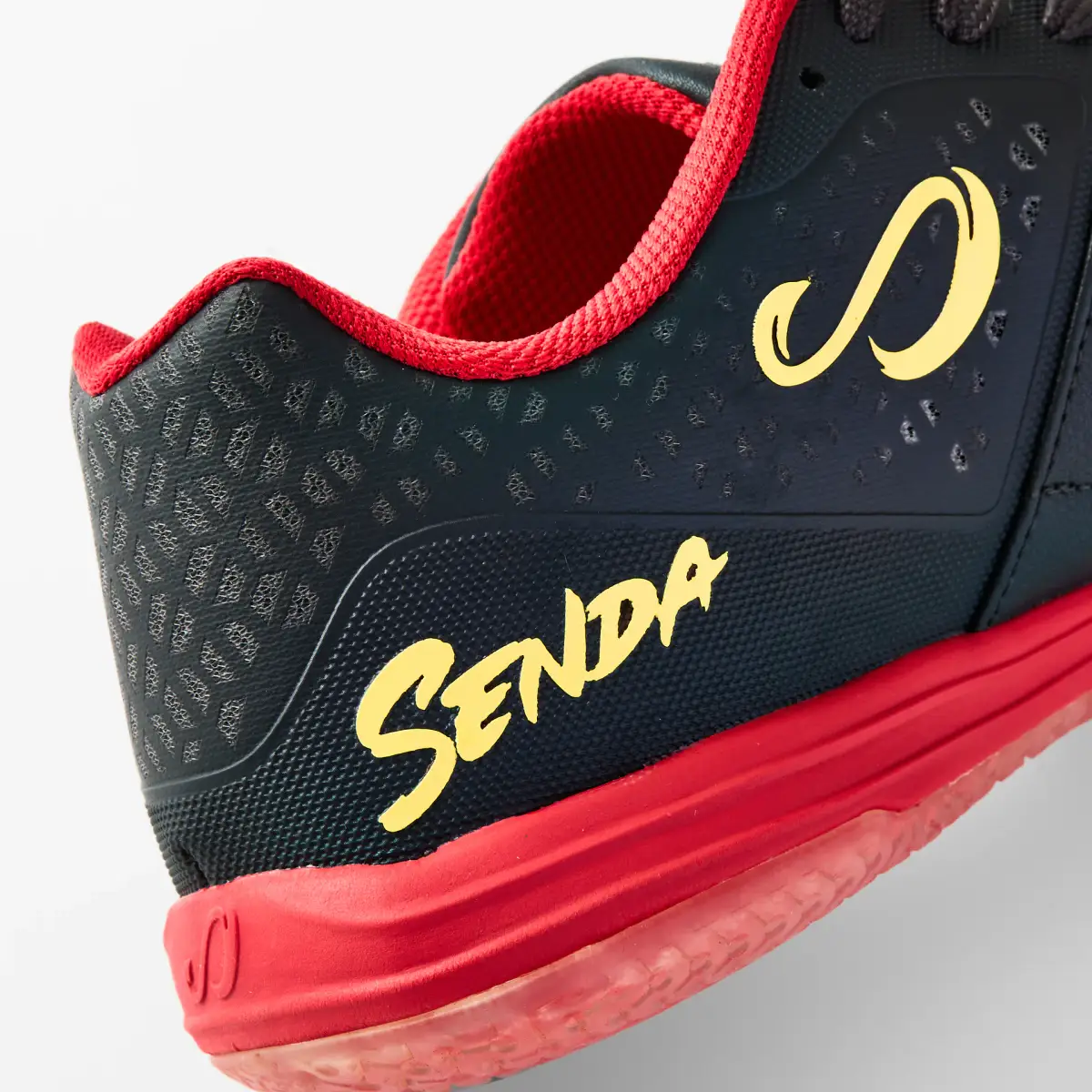Close-up of the black and red Senda Ushuaia futsal shoe showing the yellow logo, perforated upper, and red trim