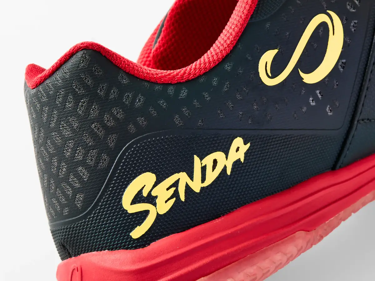Close-up of the black and red Senda Ushuaia futsal shoe showing the yellow logo, perforated upper, and red trim