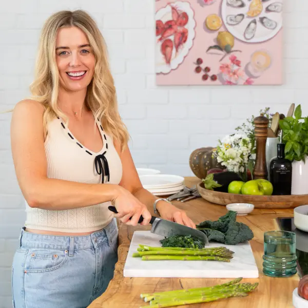 Personal-branding subject smiling while preparing food in a bright kitchen.
