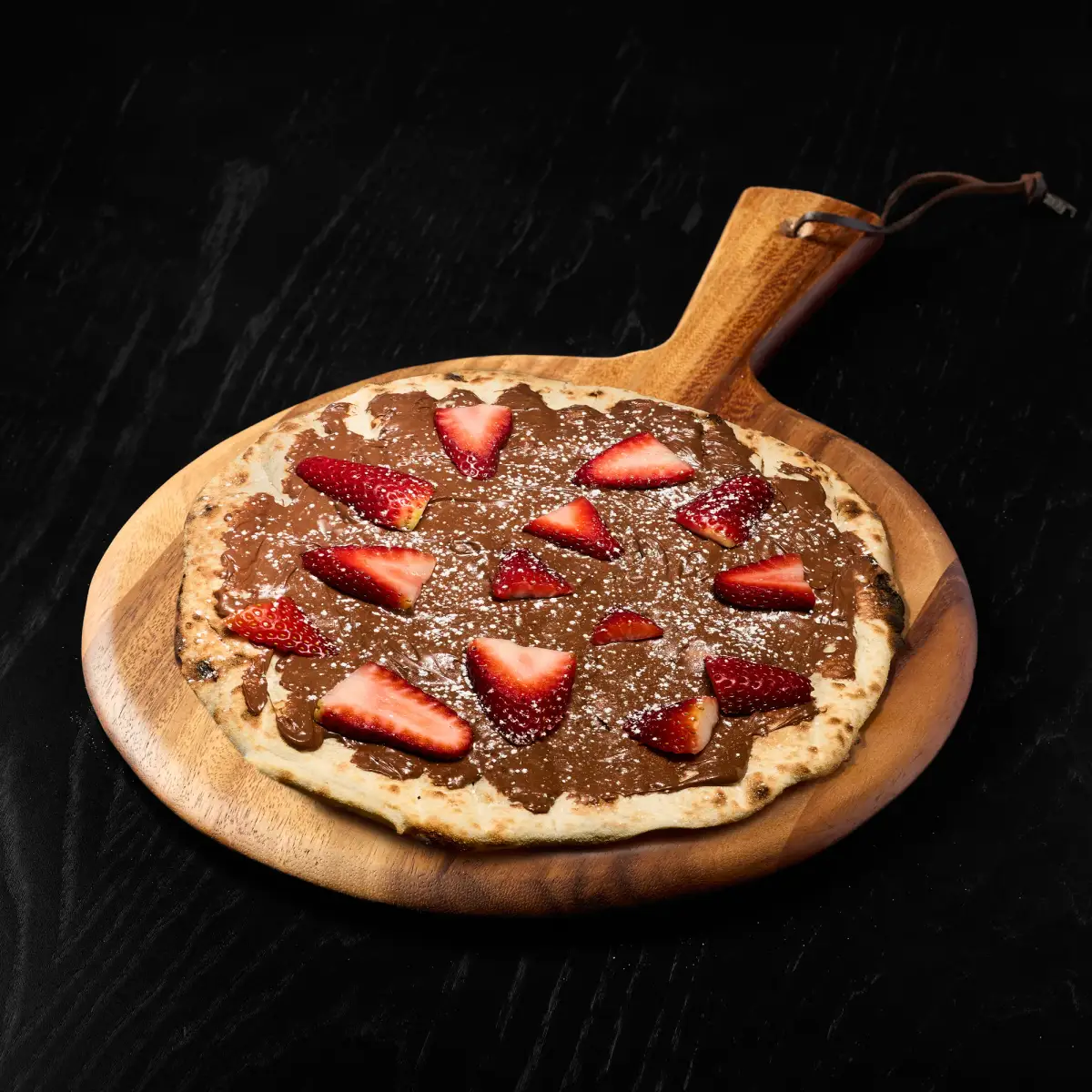 Decadent Nutella dessert pizza dusted with icing sugar and fresh strawberries from The Good Pizza