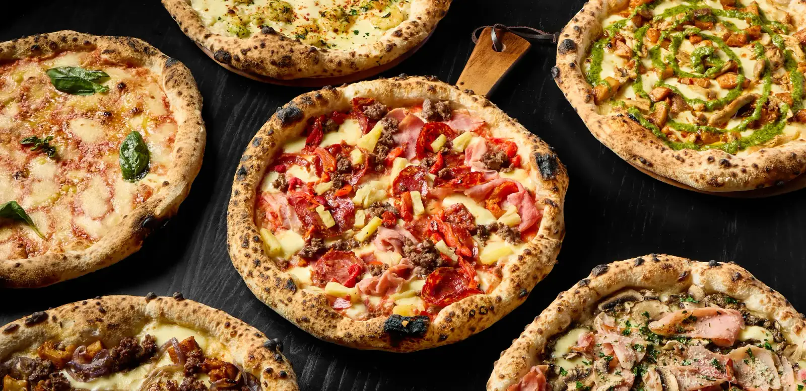Freshly baked artisan pizzas and gourmet paninis from The Good Pizza in Myaree arranged on dark surface for Uber Eats and menu marketing