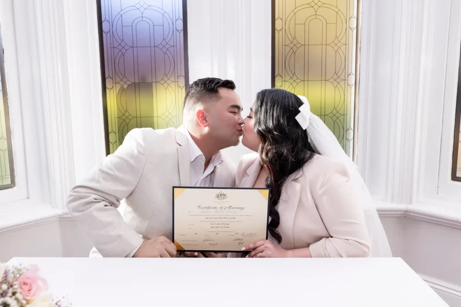 Thea and her husband kissing while holding their marriage certificate at their Perth elopement wedding.