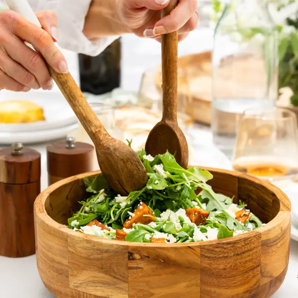 Fresh salad tossed with wooden utensils to show product use and movement.