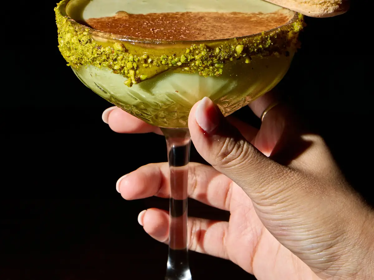 Pistachio martini-style cocktail at T.O.T.O Bar served with a macaron garnish and polished dark bar styling
