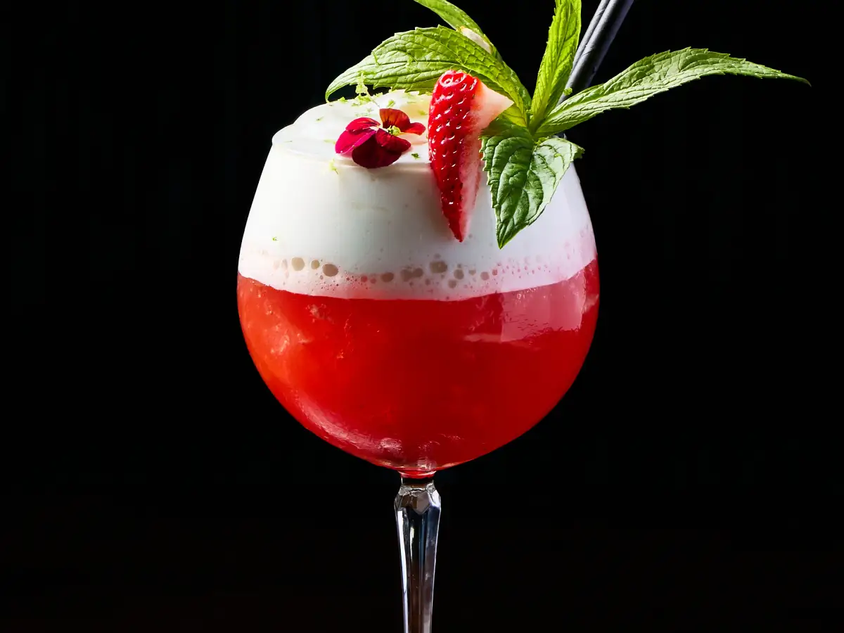 Red raspberry cocktail at T.O.T.O Bar with foam, rosemary, raspberry, and a dark studio background