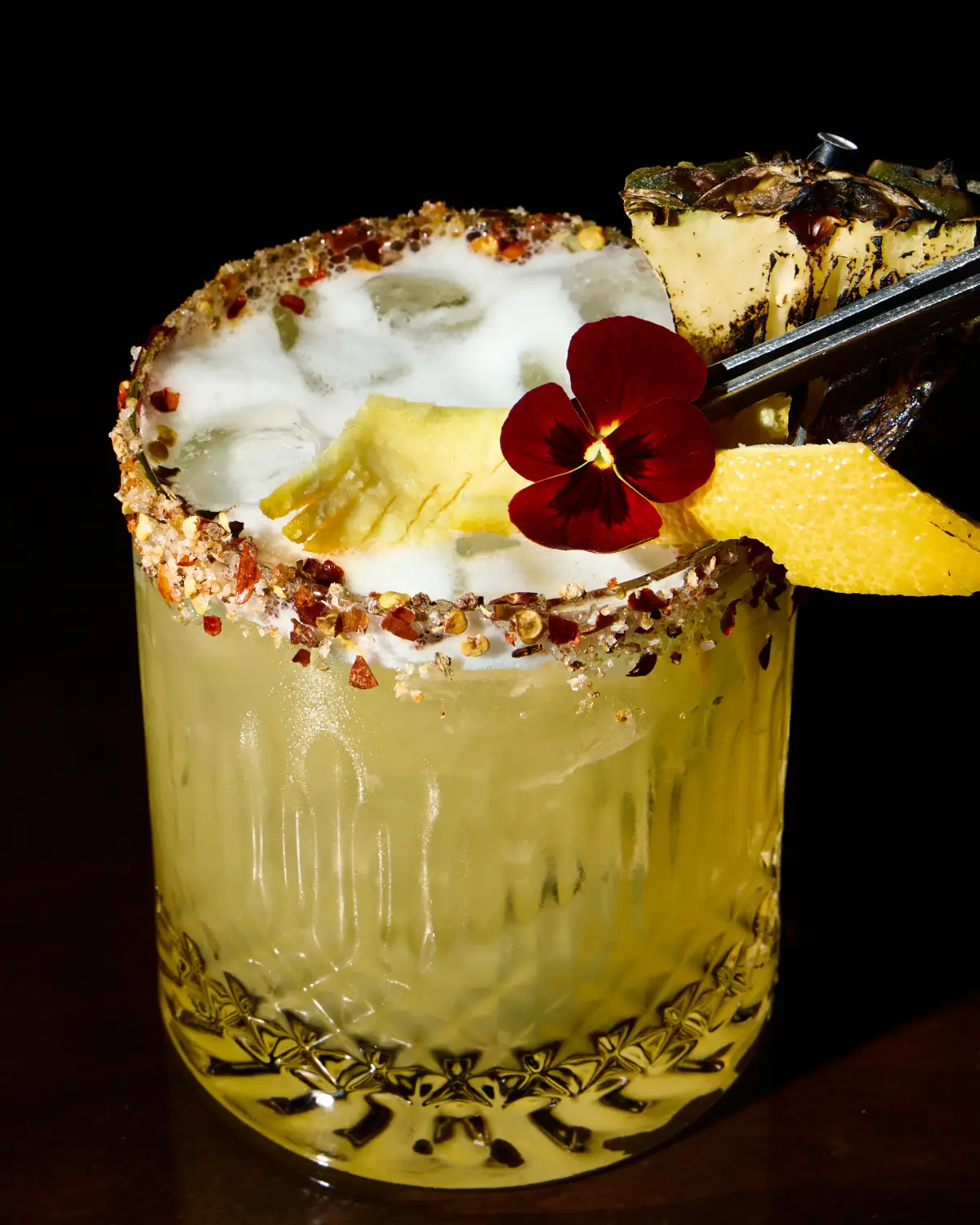 Tropical margarita-style cocktail at T.O.T.O Bar with a spiced rim, pineapple garnish, flower, and dark background