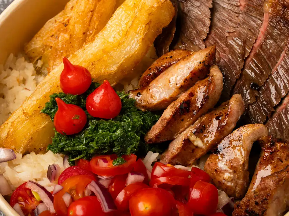 Close-up of Uai Mate BBQ carreteiro bowl with grilled rump cap steak, Brazilian sausages, chimichurri, crispy cassava, and biquinho peppers