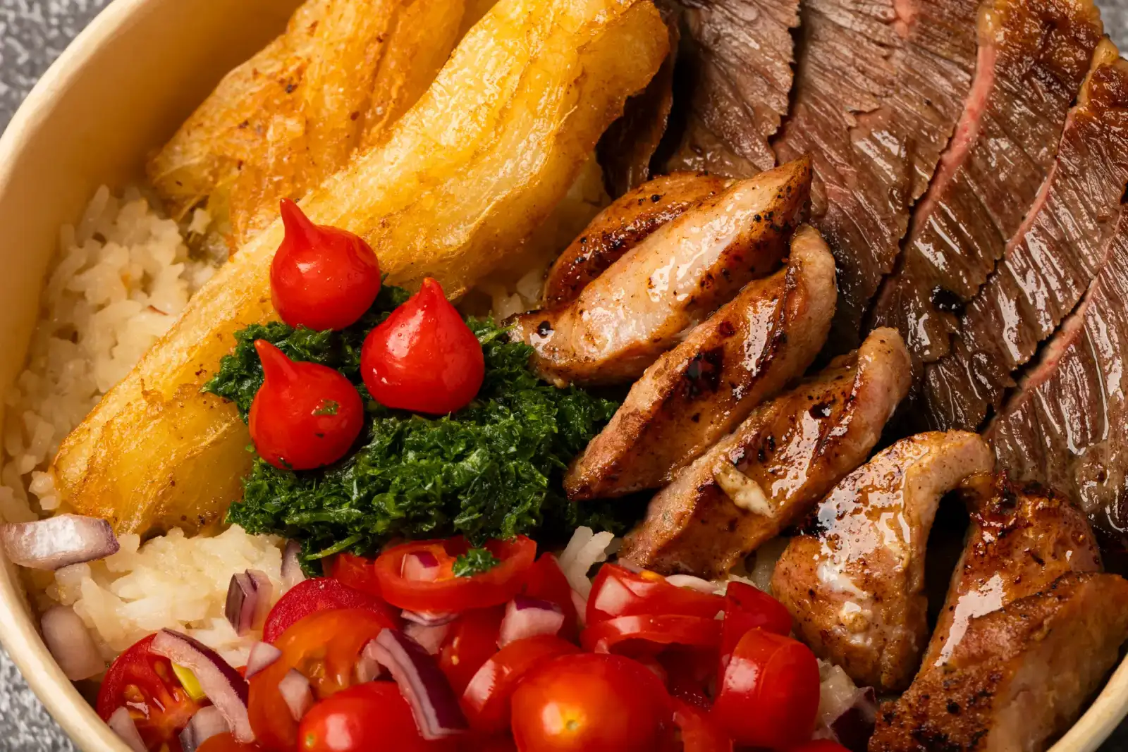 Close-up of Uai Mate BBQ carreteiro bowl with grilled rump cap steak, Brazilian sausages, chimichurri, crispy cassava, and biquinho peppers