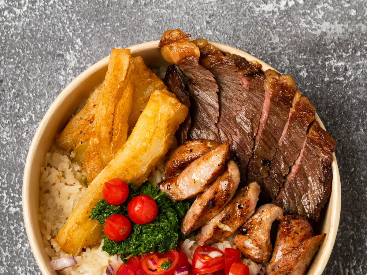 Overhead view of Uai Mate BBQ carreteiro plate with sliced steak, sausages, cassava, chimichurri, and tomato salsa on rice