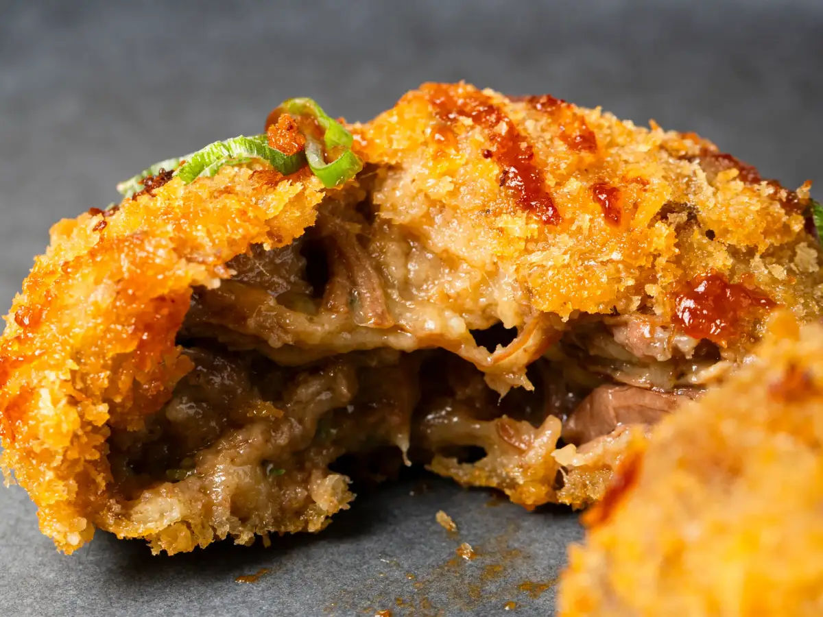 Uai Mate beef ribs croquete broken open to show pulled meat filling with spicy BBQ sauce and spring onion garnish