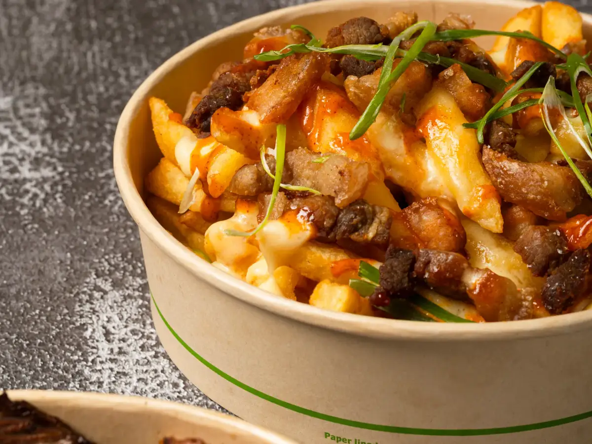 Close-up of Uai Mate holy crack fries loaded with crispy pork belly, melted cheese, chipotle mayo, and spring onions