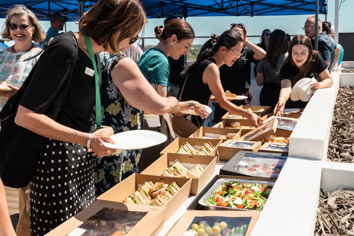 Guests selecting boxed sandwiches and salads from a catering table during a Vera Living rooftop event