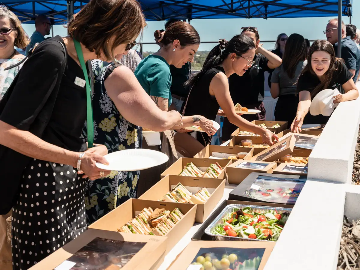 Guests selecting boxed sandwiches and salads from a catering table during a Vera Living rooftop event