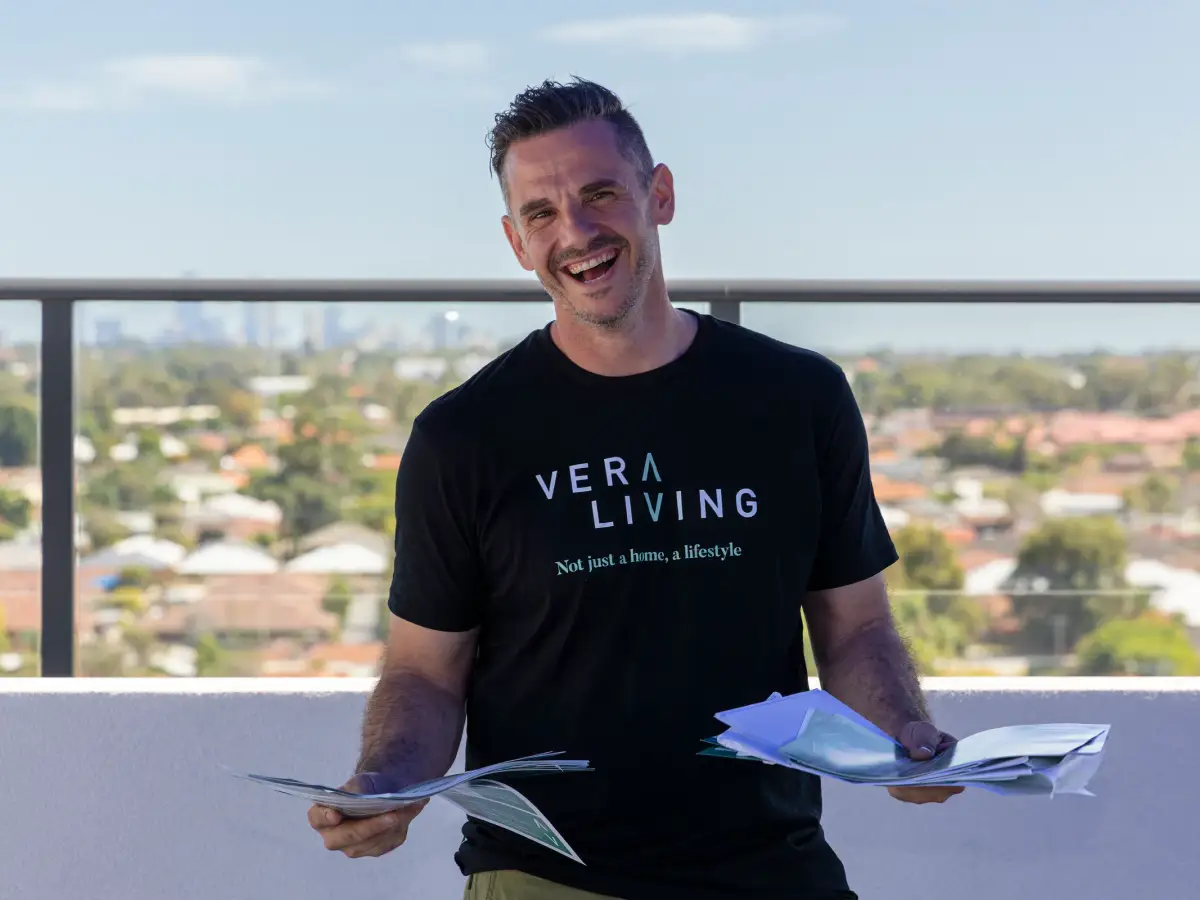 Vera Living team member holding brochures on a rooftop terrace with the Cannington skyline blurred behind him