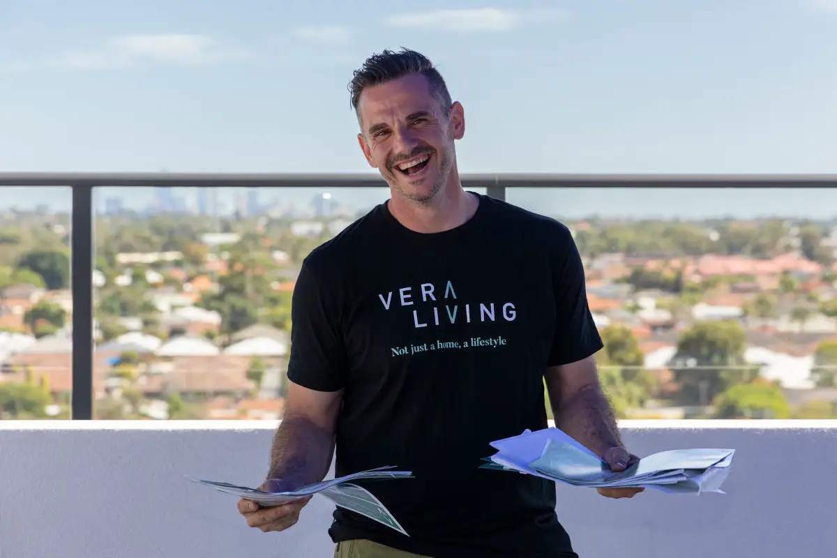 Vera Living team member holding brochures on a rooftop terrace with the Cannington skyline blurred behind him