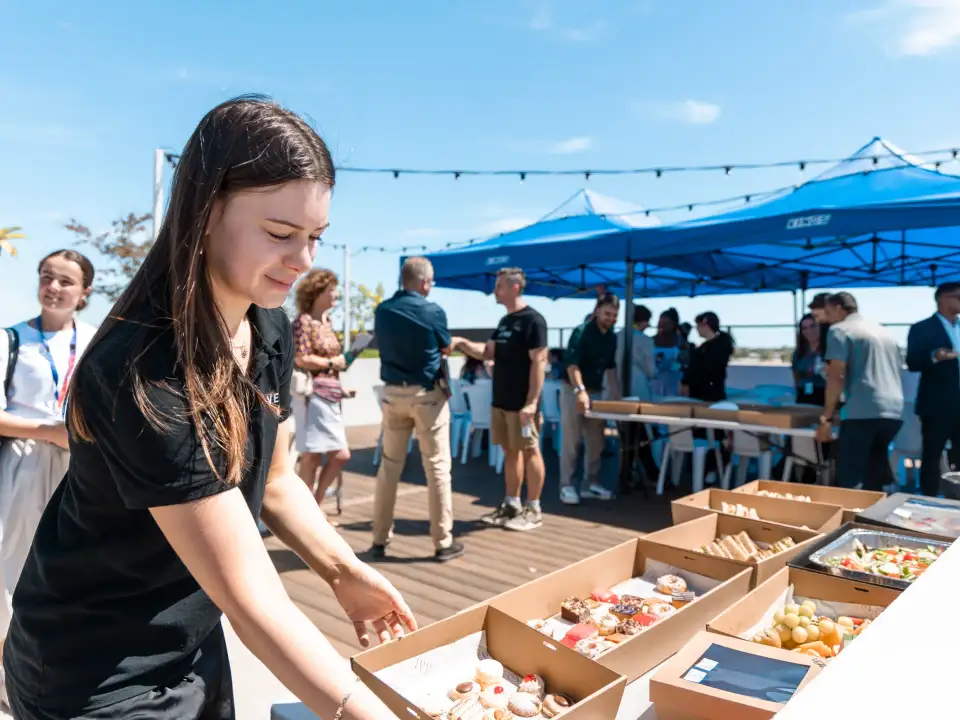 Vera Living staff member arranging catering boxes on a rooftop table while guests gather under blue marquees in Cannington