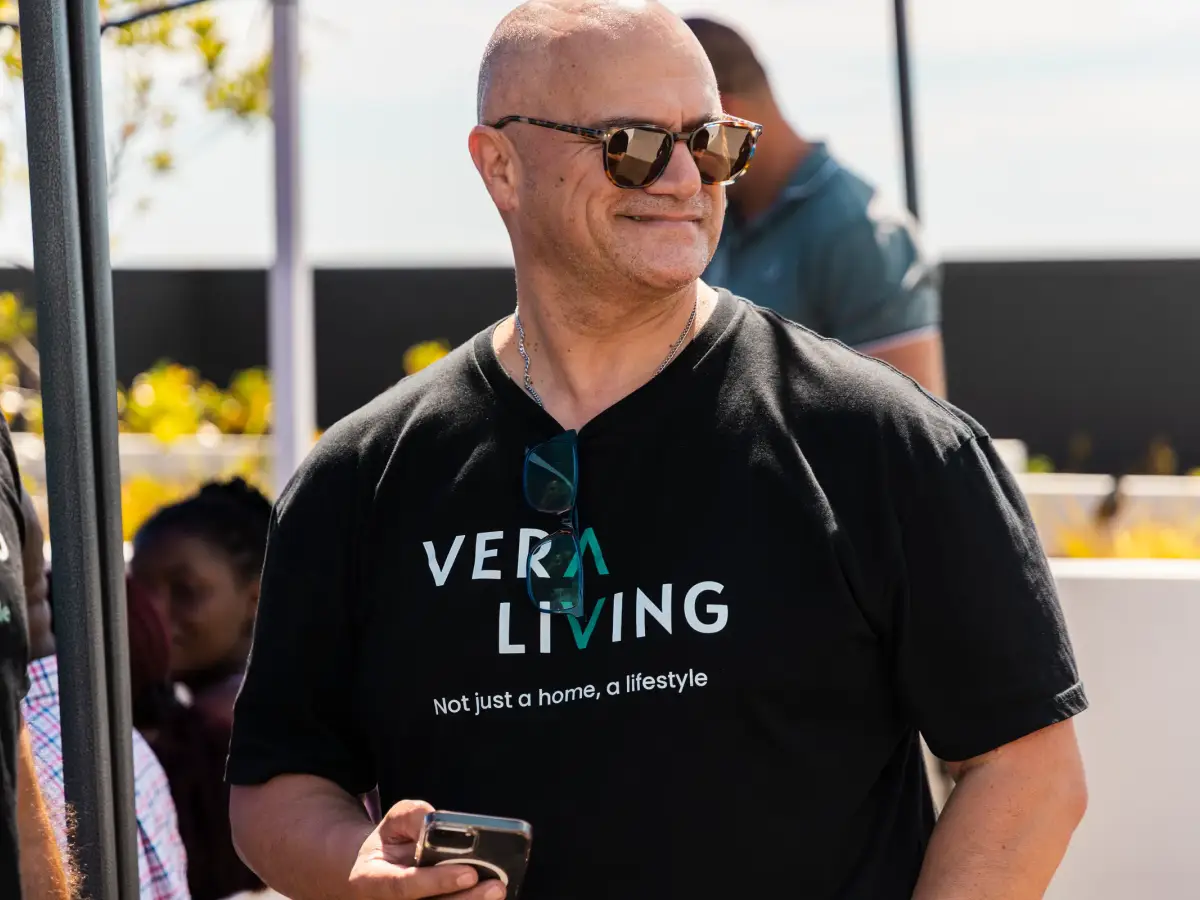 Man in sunglasses wearing a Vera Living shirt and holding a phone during a rooftop event