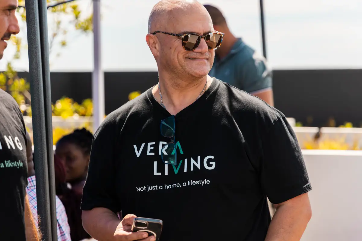 Man in sunglasses wearing a Vera Living shirt and holding a phone during a rooftop event