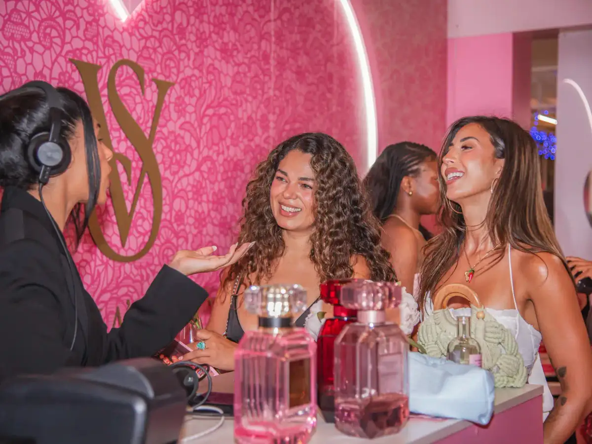 DJ and guests laughing at the fragrance counter with Victoria's Secret Bombshell bottles on display