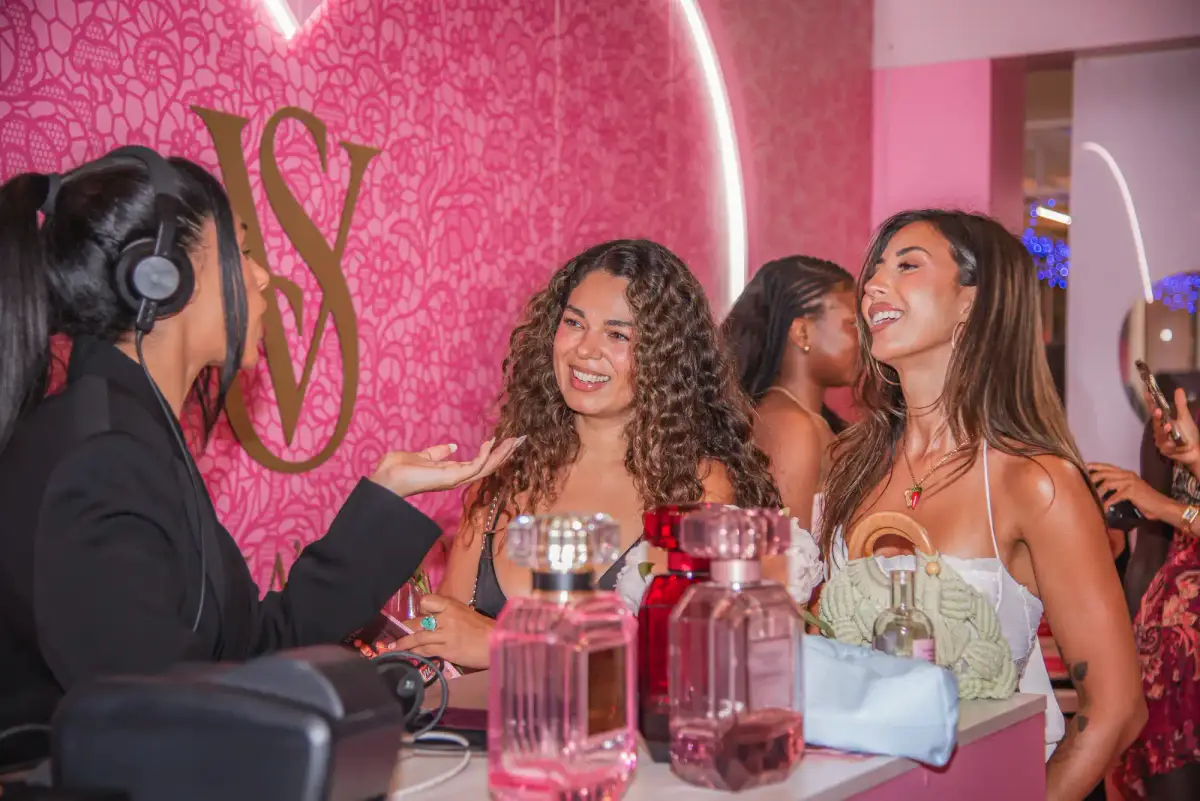 DJ and guests laughing at the fragrance counter with Victoria's Secret Bombshell bottles on display