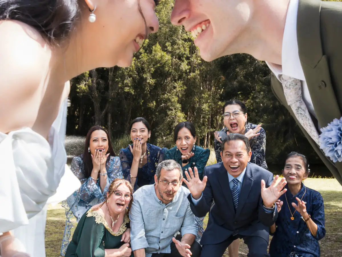 Wedding couple surrounded by family reactions during portraits after the ceremony