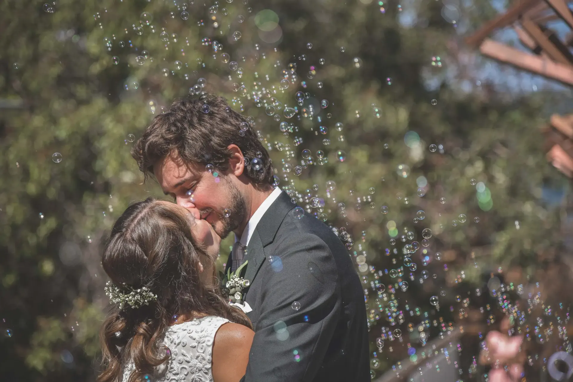 Wedding couple kissing beneath bubbles during a candid celebration moment.