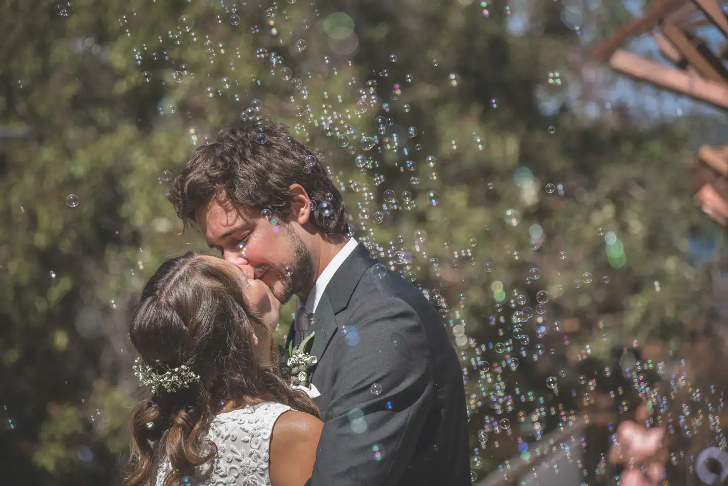 Wedding couple kissing beneath bubbles as their celebration continues.