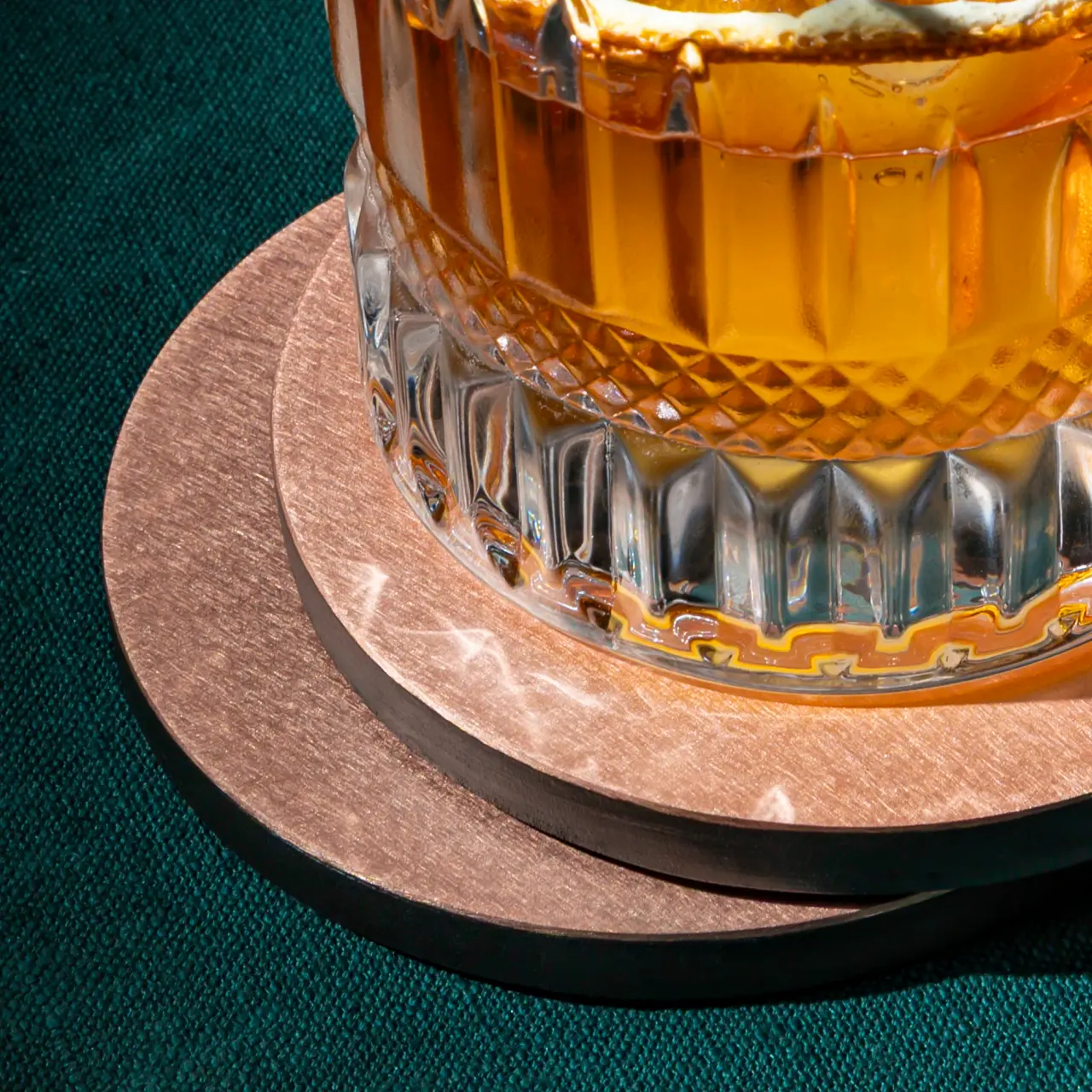 Close-up lifestyle product image of a whisky glass on stacked metallic coasters
