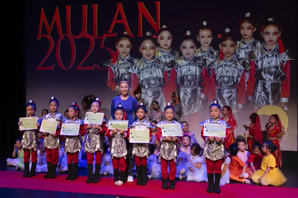 Dance instructor and students holding certificates on stage in front of a Mulan 2025 projection