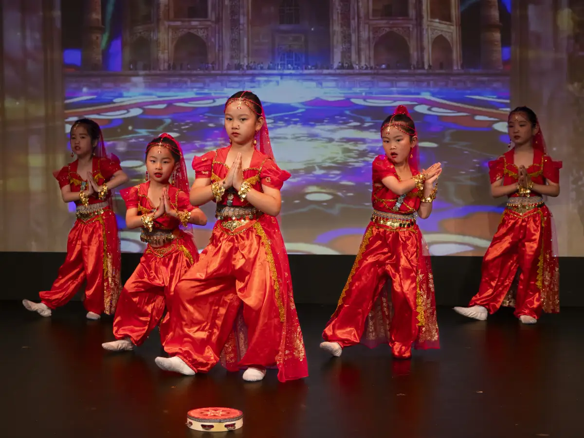 Five young dancers performing in bright red costumes on a theatre stage during a Yup Dance Academy showcase