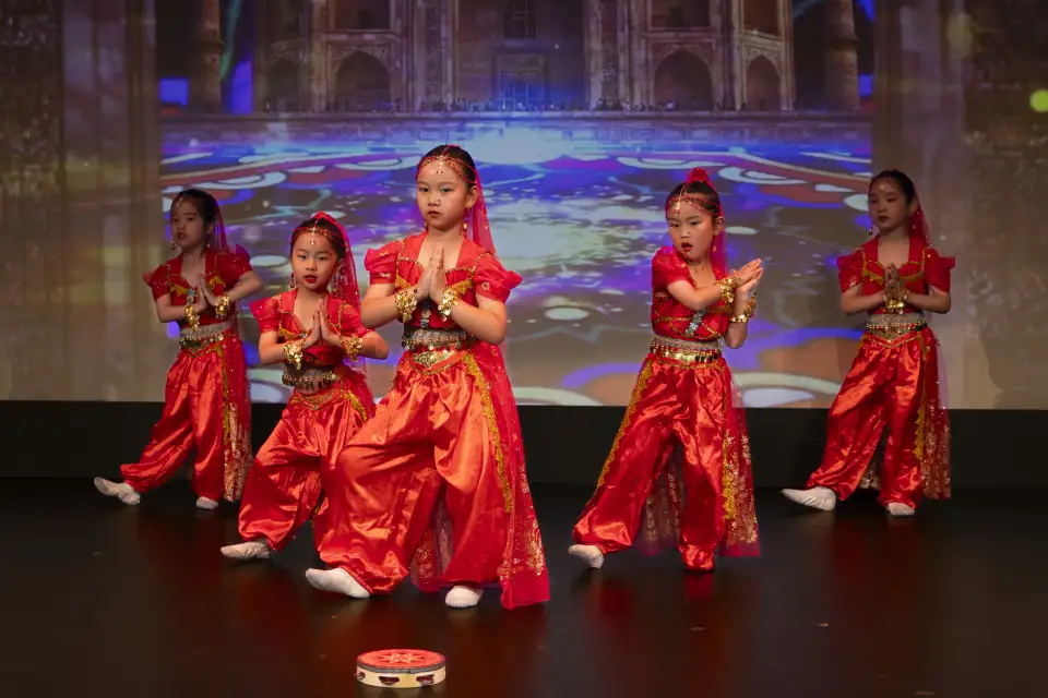 Five young dancers performing in bright red costumes on a theatre stage during a Yup Dance Academy showcase